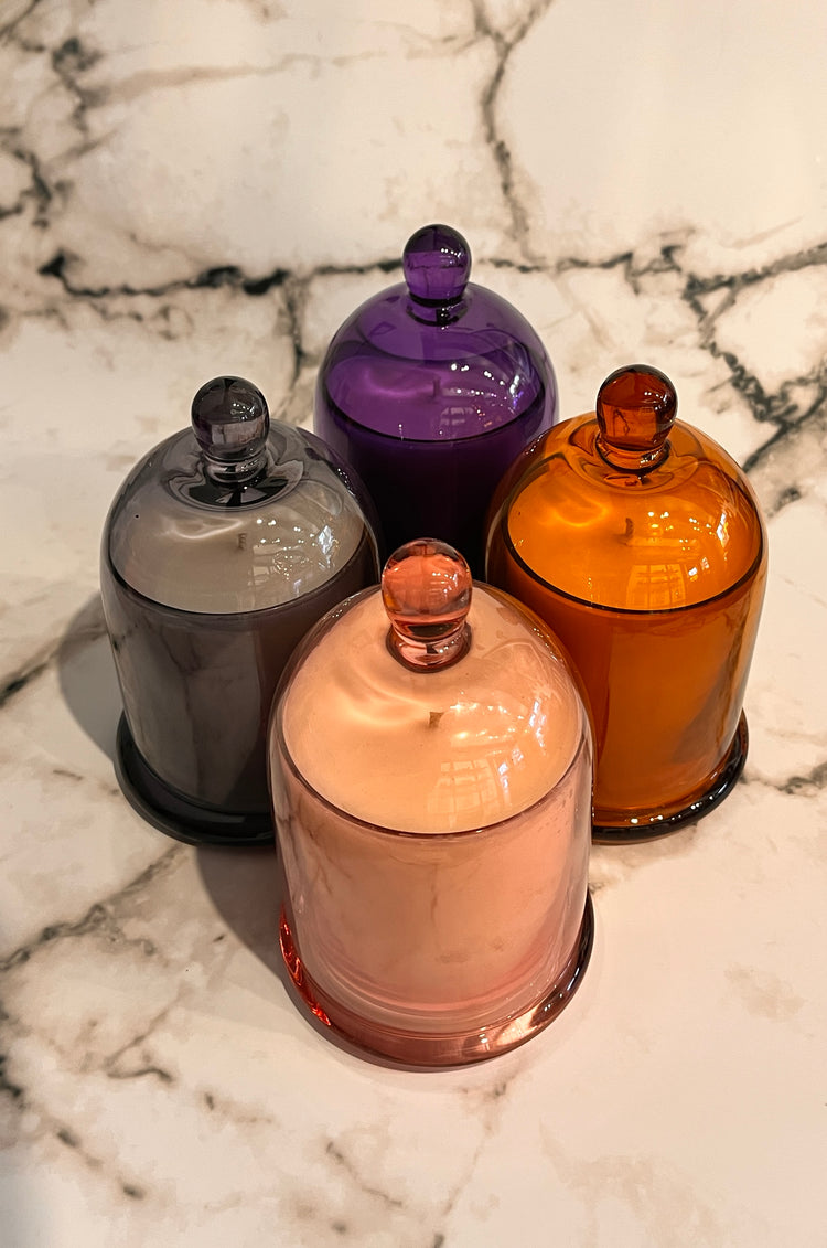 Four glass cloche bell jar candles in a diamond shape, colours of pink, grey, purple and amber. 
